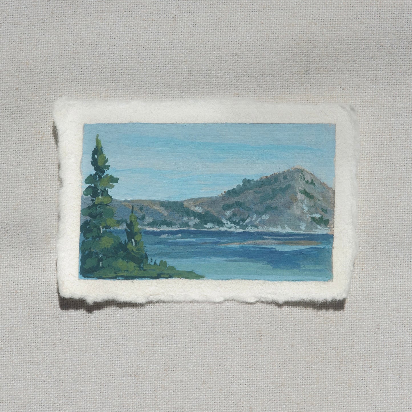 Small gouache painting of pine tree, crater lake, and jagged mountains by Laura Van Moorleghem from Crater Lake National Park
