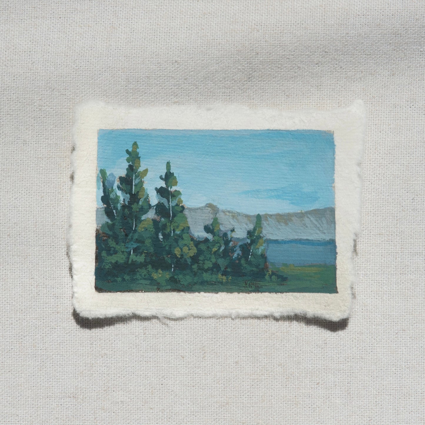 Small gouache painting of crater lake blues with pine tree and mountains by Laura Van Moorleghem from Crater Lake National Park