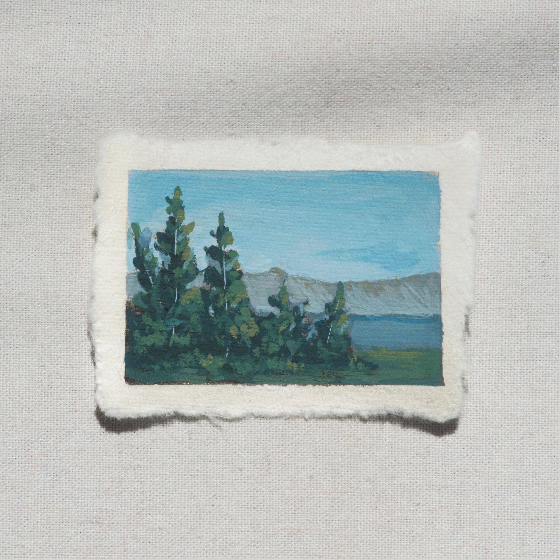 Small gouache painting of crater lake blues with pine tree and mountains by Laura Van Moorleghem from Crater Lake National Park