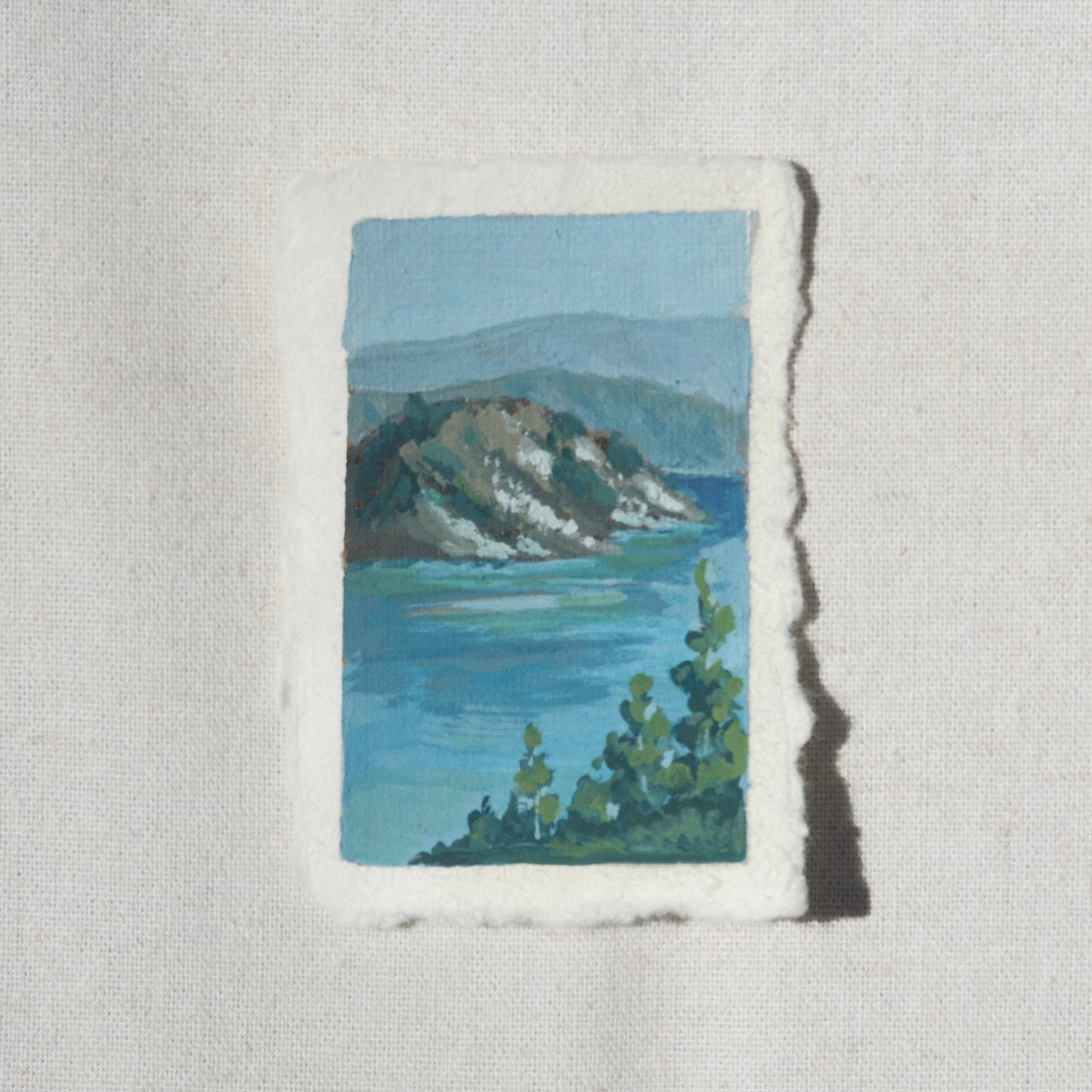 Miniature landscape gouache painting of crater lake blues with wizard island and mountains in the backdrop by Laura Van Moorleghem from Crater Lake National Park