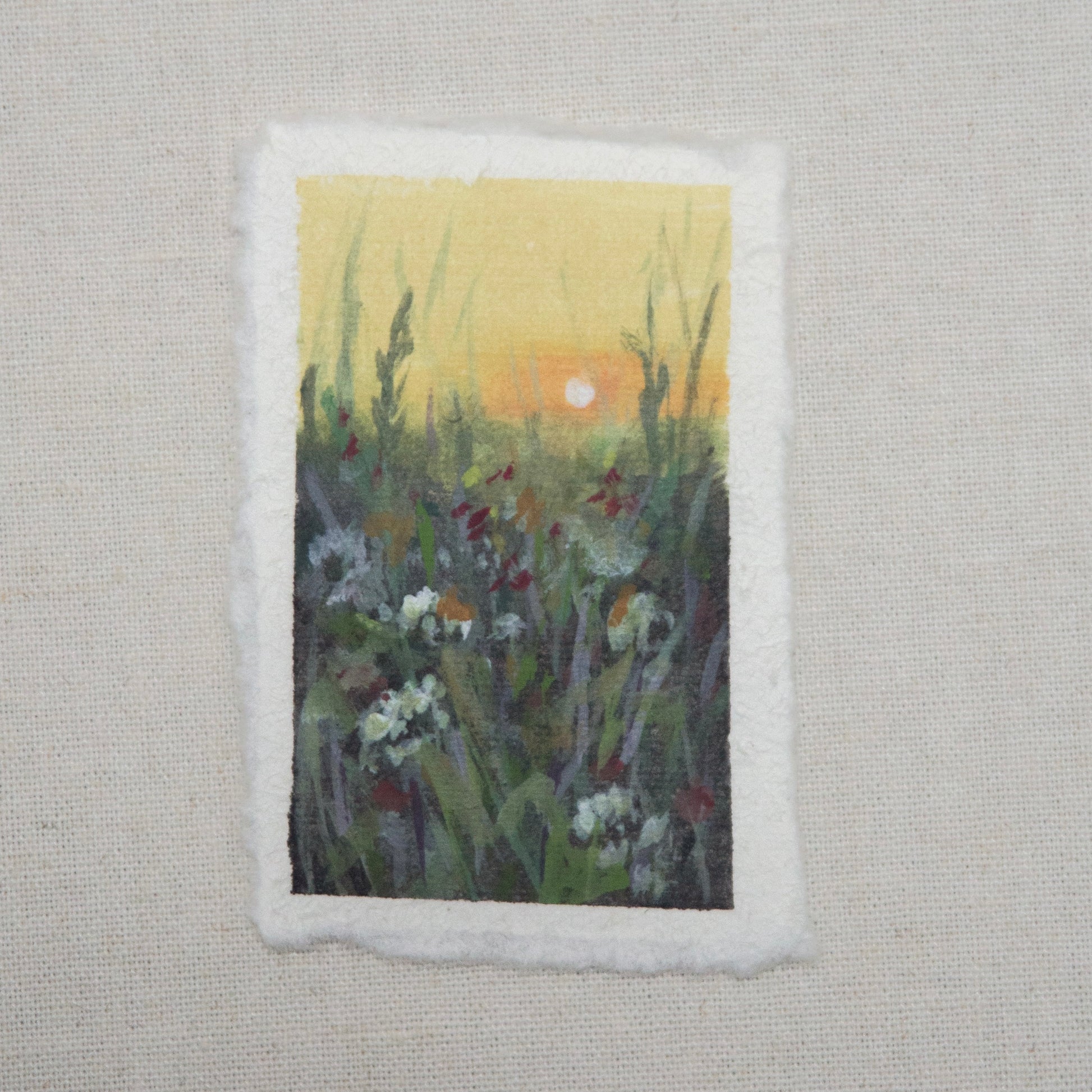 A small painting featuring a sunset over a field of flowers, painted with gouache and acrylic on cotton rag paper with a deckled edge by artist Laura van Moorleghem