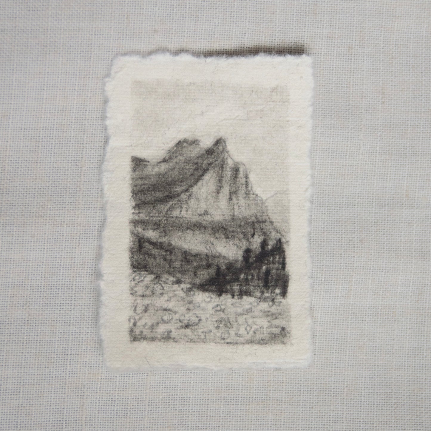 A charcoal sketch of a view from 'going to the sun road' in Glacier National Park on deckled edge paper, with visible strokes and shading created by artist Laura Van Moorleghem