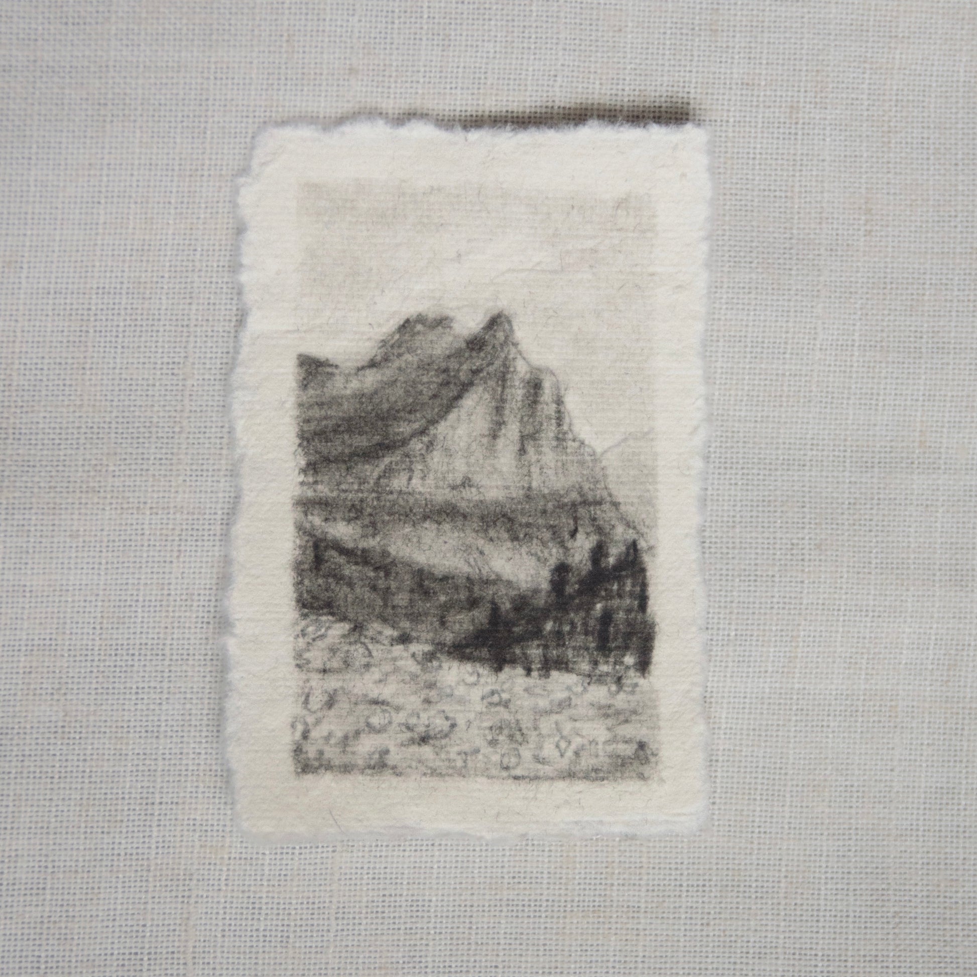 A charcoal sketch of a view from 'going to the sun road' in Glacier National Park on deckled edge paper, with visible strokes and shading created by artist Laura Van Moorleghem