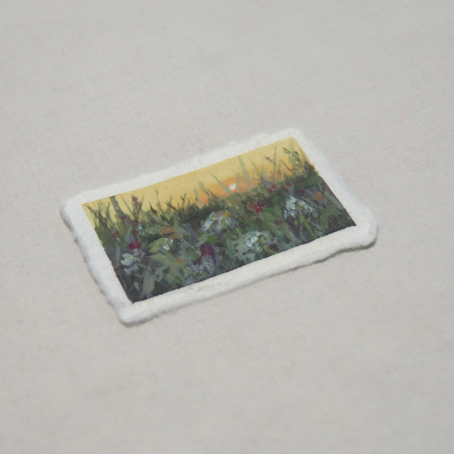 miniature landscape depicting floral field during golden hour on deckled edge paper