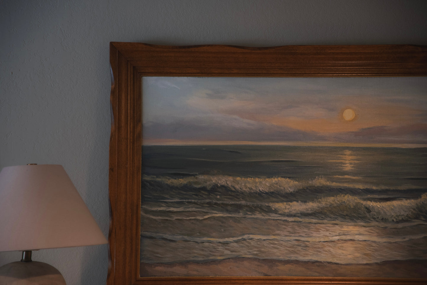 A framed ocean artwork depicting a serene coastal scene with a vintage wood frame, displayed in a room next to a lamp.