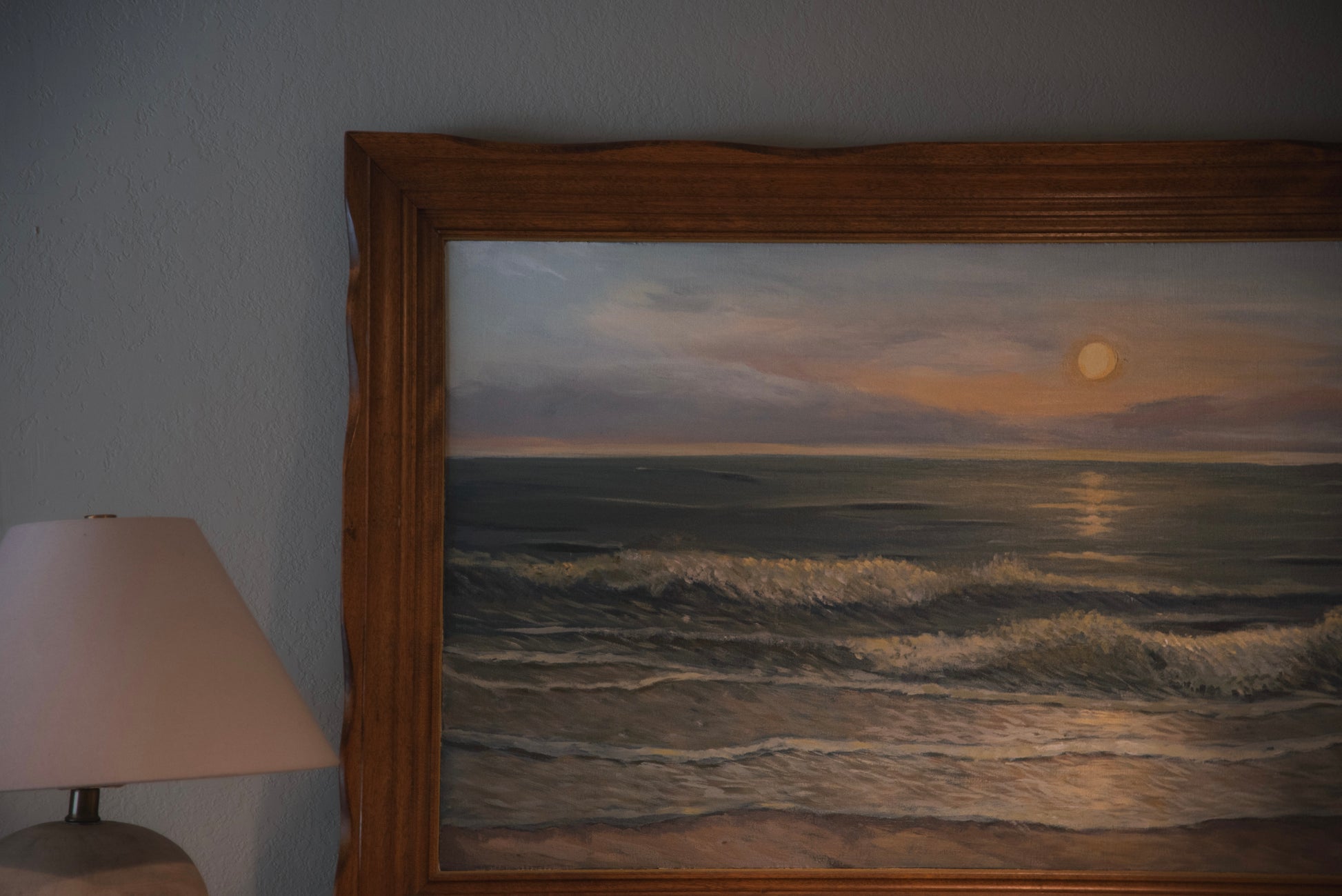 A framed ocean artwork depicting a serene coastal scene with a vintage wood frame, displayed in a room next to a lamp.