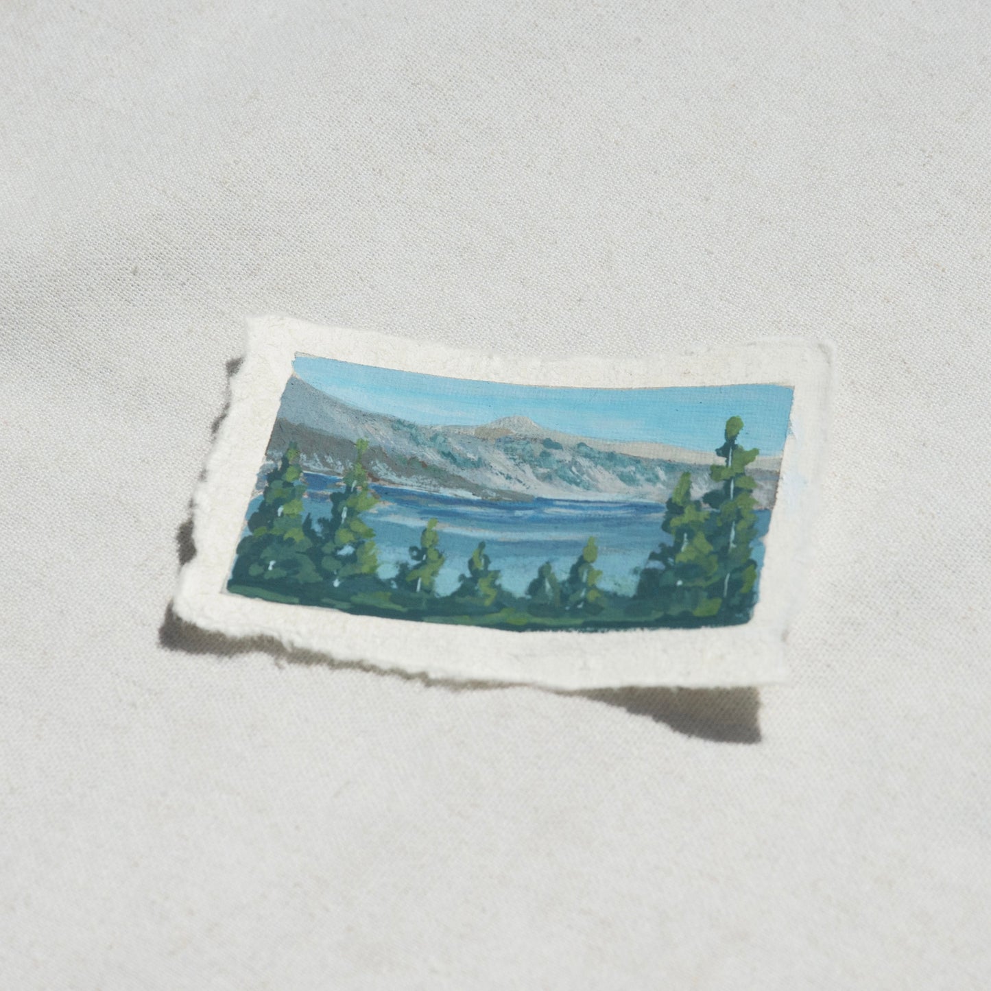 Side profile of the lake, pine trees, and mountains in Crater Lake National Park painting on deckled edge 100% cotton rag paper