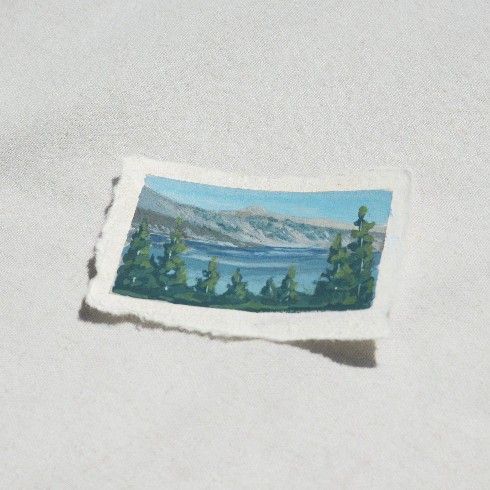 Side profile of the lake, pine trees, and mountains in Crater Lake National Park painting on deckled edge 100% cotton rag paper