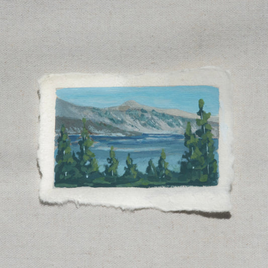 Mini gouache painting of the mountains, pine trees, and vibrant blue water of Crater Lake by Laura Van Moorleghem from Crater Lake National Park