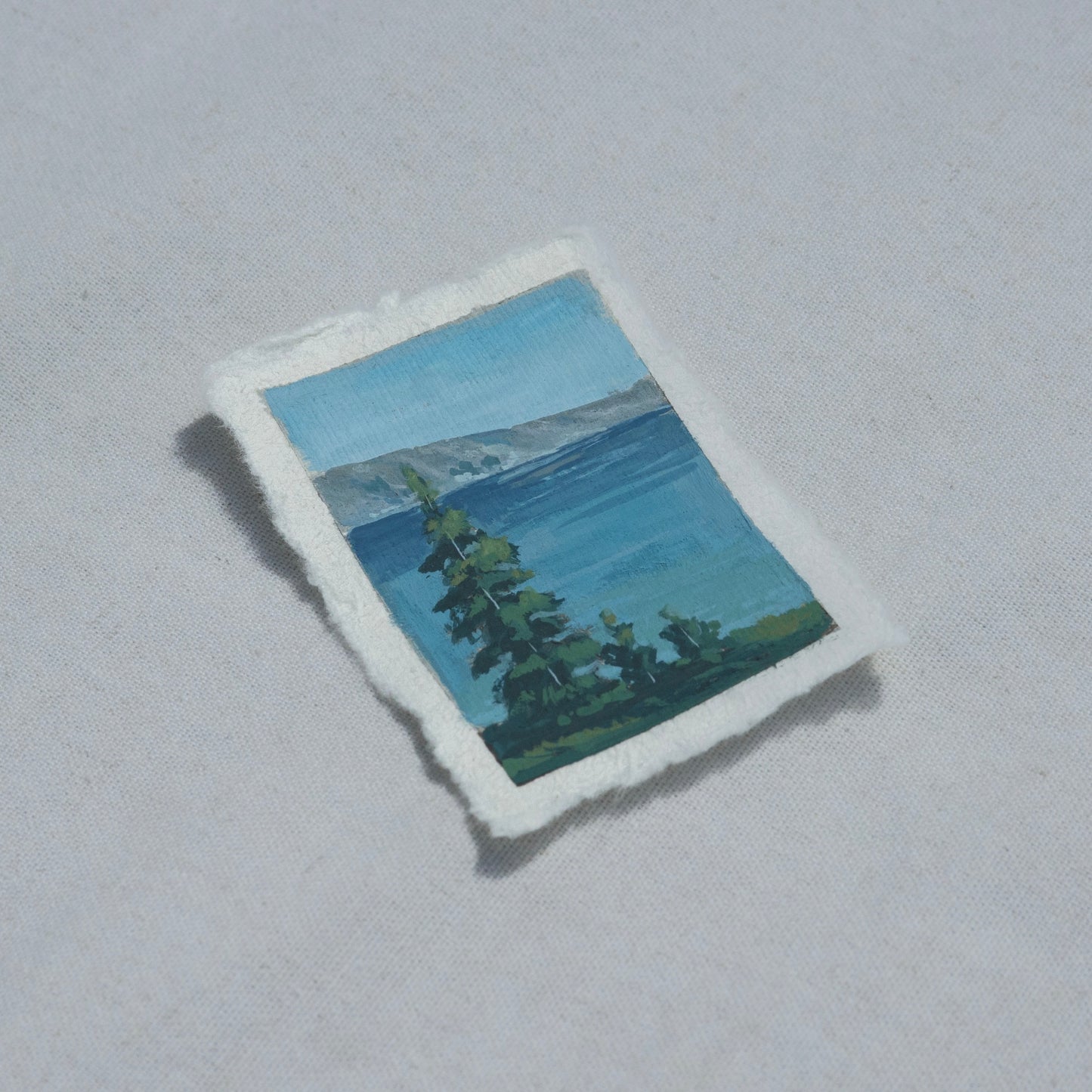 Side profile of trees overlooking crater lake with mountains in Crater Lake National Park painting on deckled edge 100% cotton rag paper