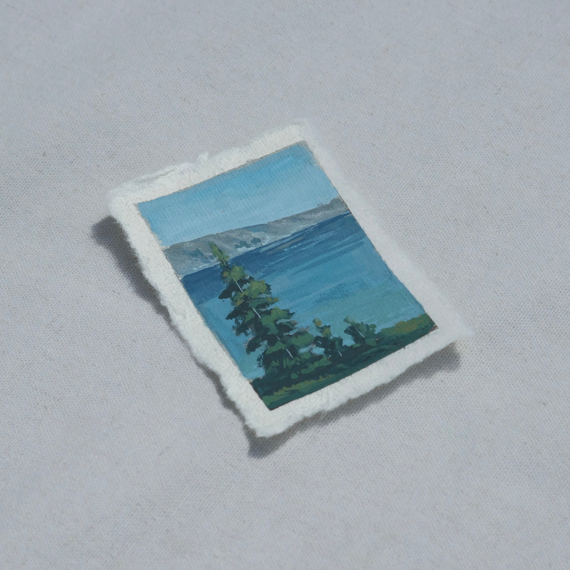 Side profile of trees overlooking crater lake with mountains in Crater Lake National Park painting on deckled edge 100% cotton rag paper