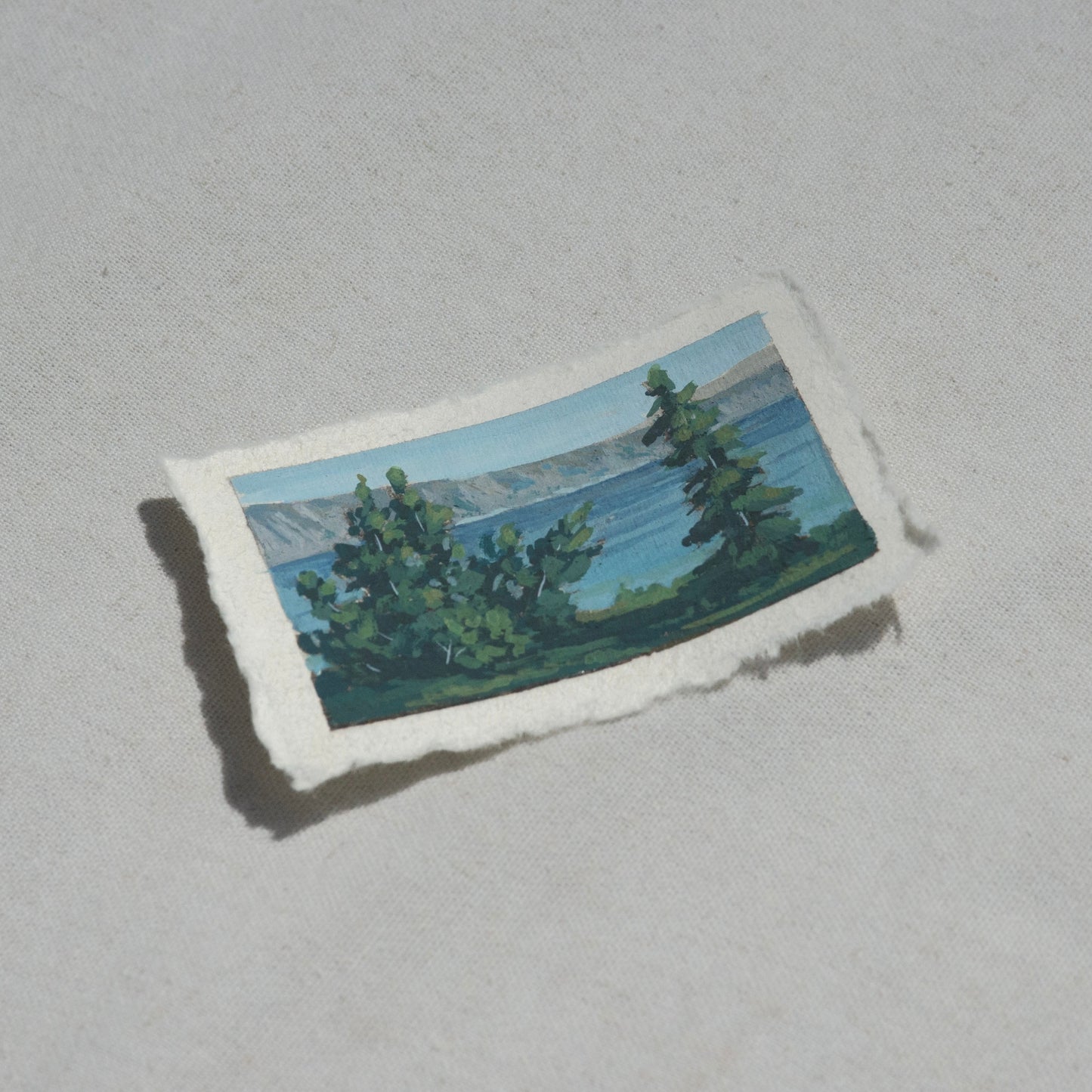 Side profile of Crater Lake National Park of mountains, lake, and pine trees painting on deckled edge 100% cotton rag paper