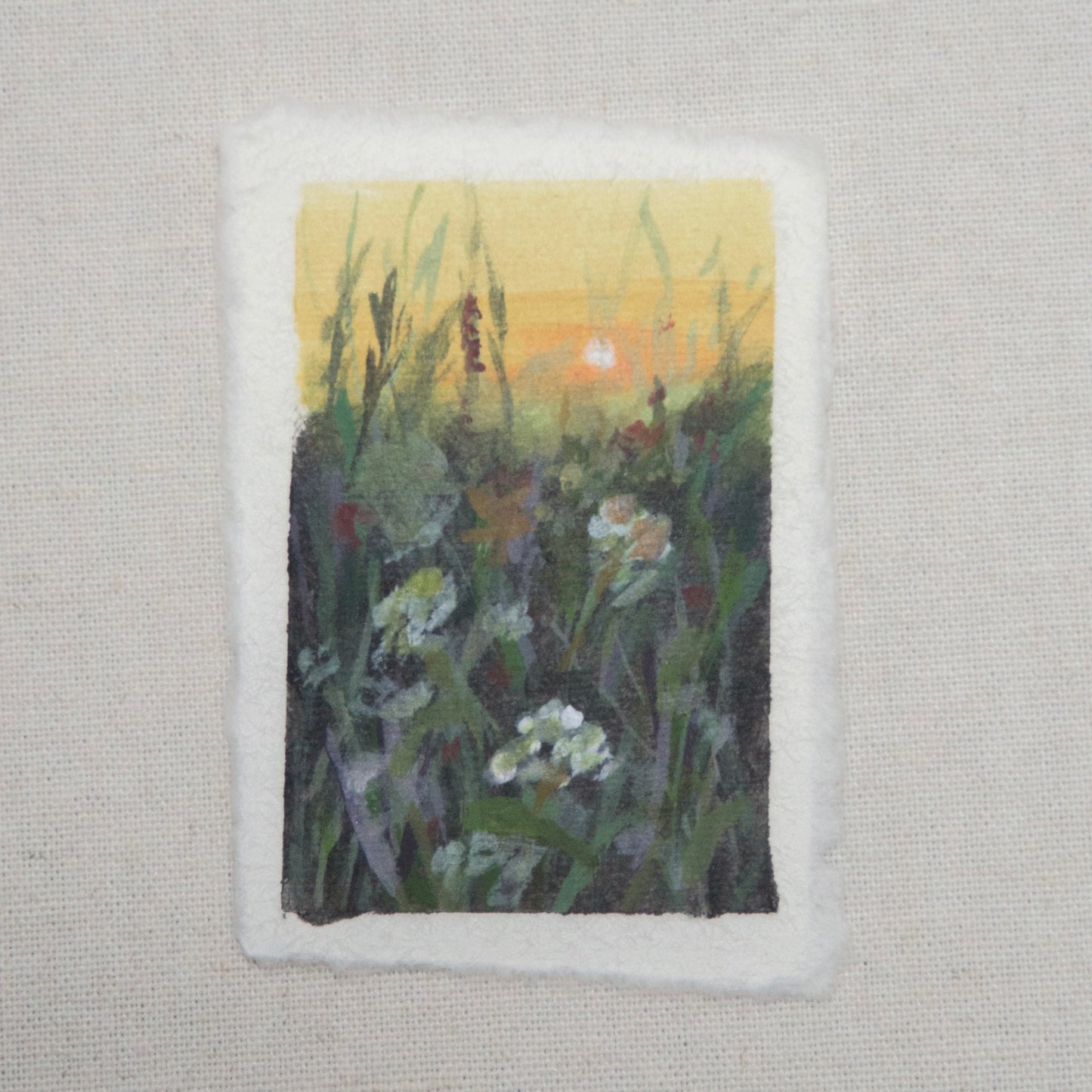 A small artwork titled 'In Bloom', featuring a floral scene with gouache and acrylic paints on cotton rag paper with a deckled edge by artist Laura Van Moorleghem