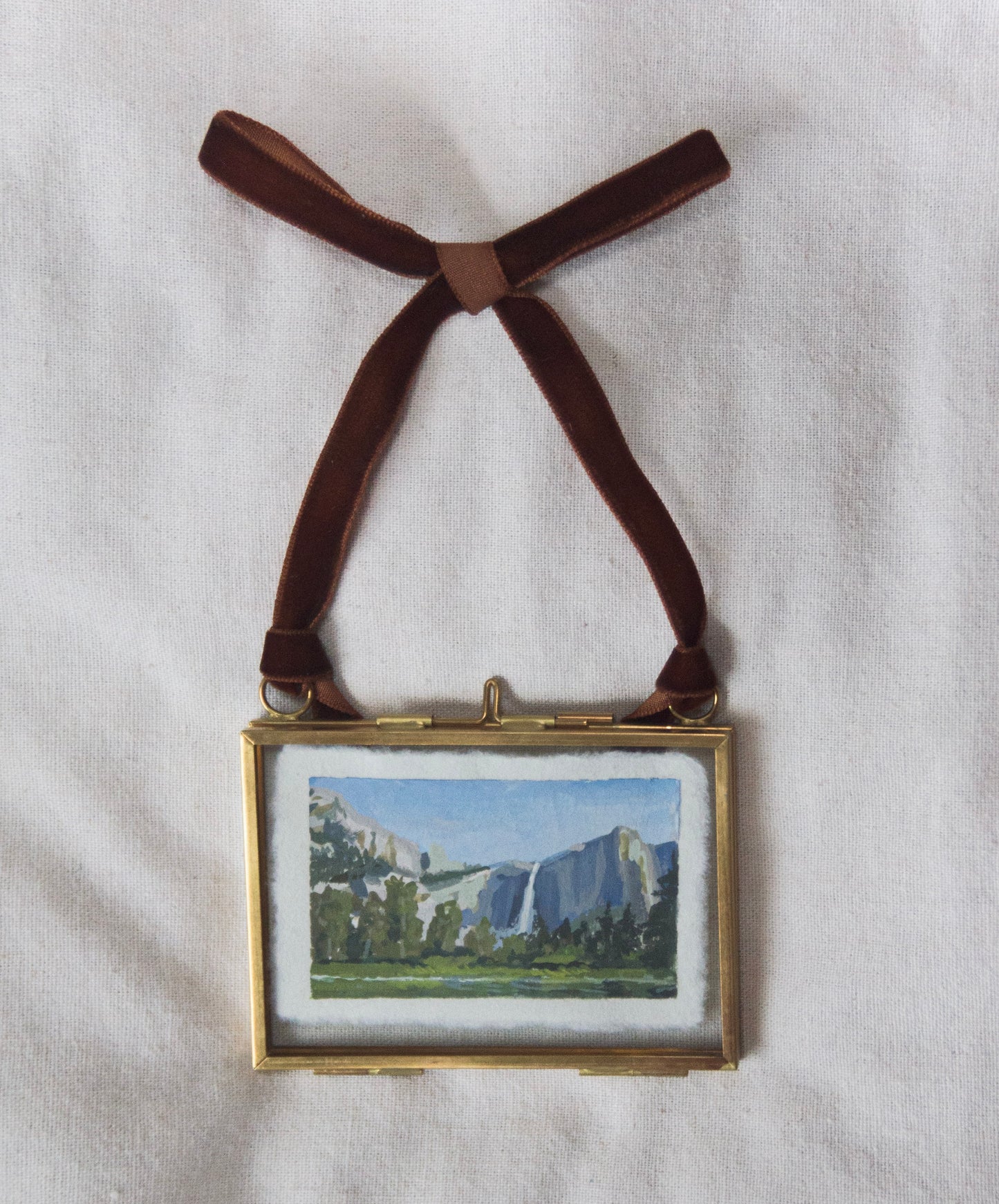 Small Yosemite landscape painting of Upper Yosemite falls in a gold frame with a brown ribbon on a white background