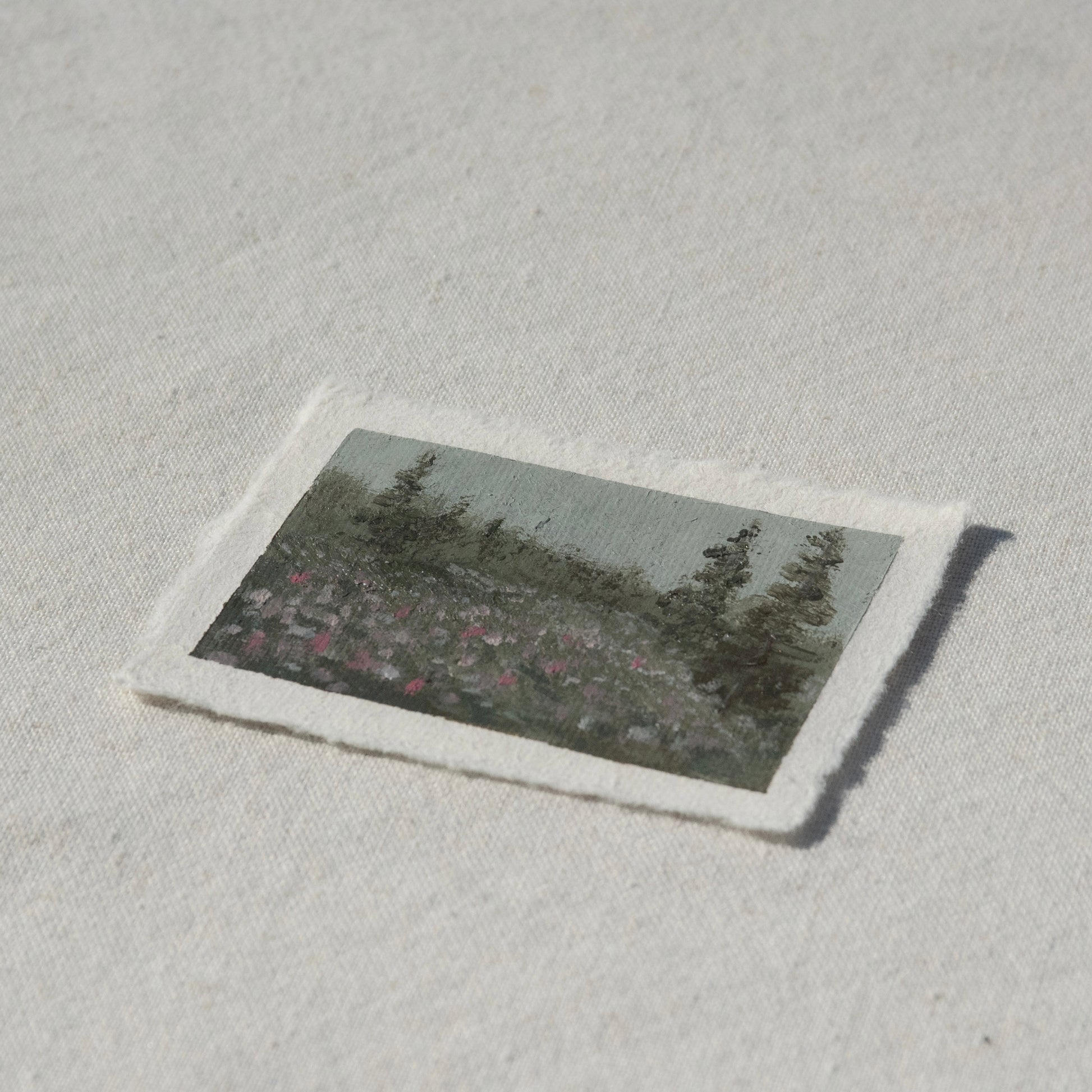 Side profile of hillside filled with colorful wildflowers and pine trees painting on deckled edge 100% cotton rag paper 